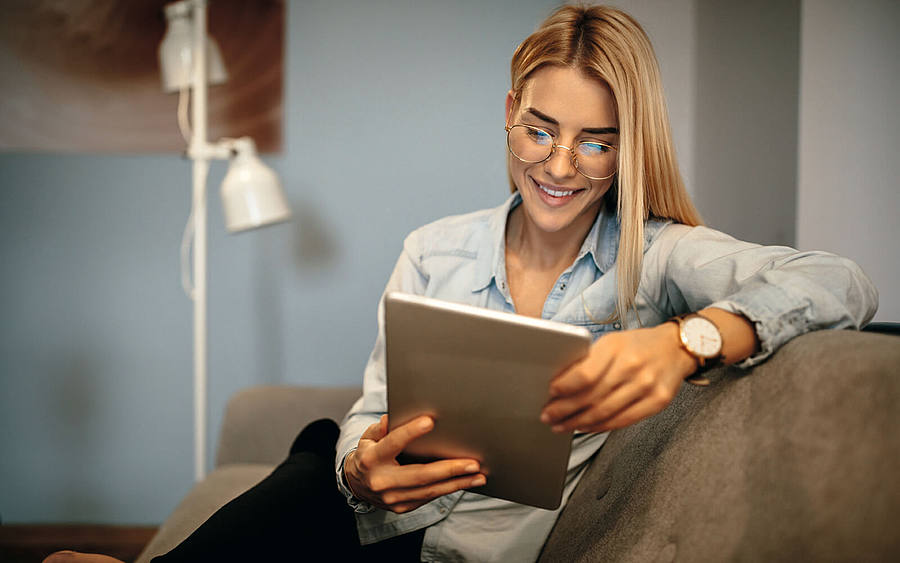 Eine blonde Frau mit Brille betrachtet ein Tablet.