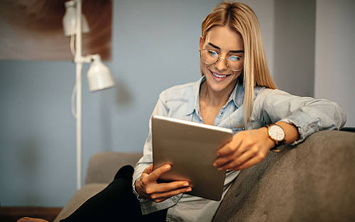 Eine blonde Frau mit Brille betrachtet ein Tablet.