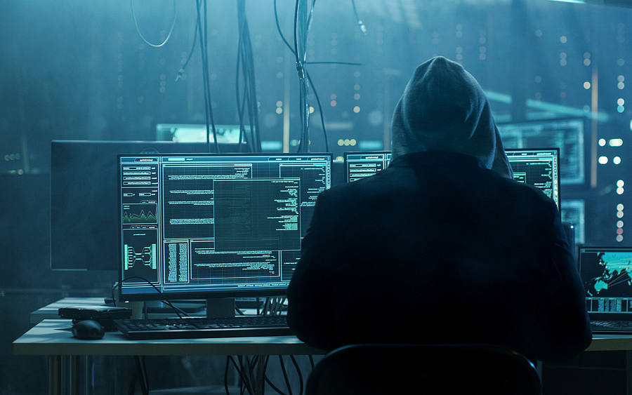 Rücken eines Hackers vor diversen PCs