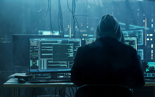 Rücken eines Hackers vor diversen PCs