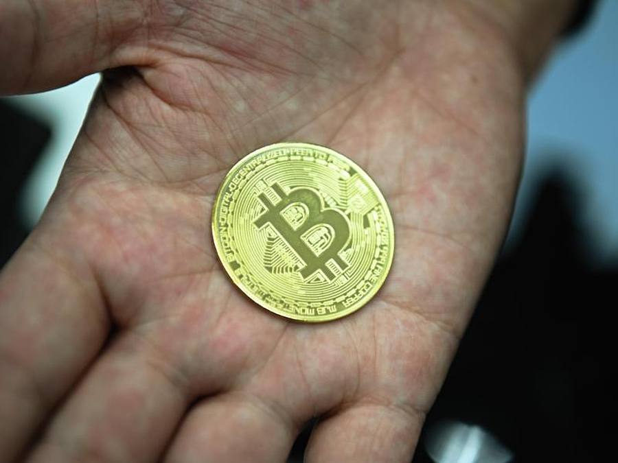 Ein Mann mit eine nachgemachter Münze mit dem Bitcoin-Logo. Foto: Nicolas Armer/dpa