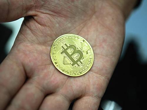 Ein Mann mit eine nachgemachter Münze mit dem Bitcoin-Logo. Foto: Nicolas Armer/dpa