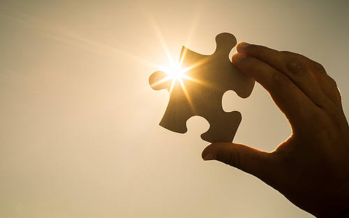 Hand hält Puzzleteil gegen die Sonne