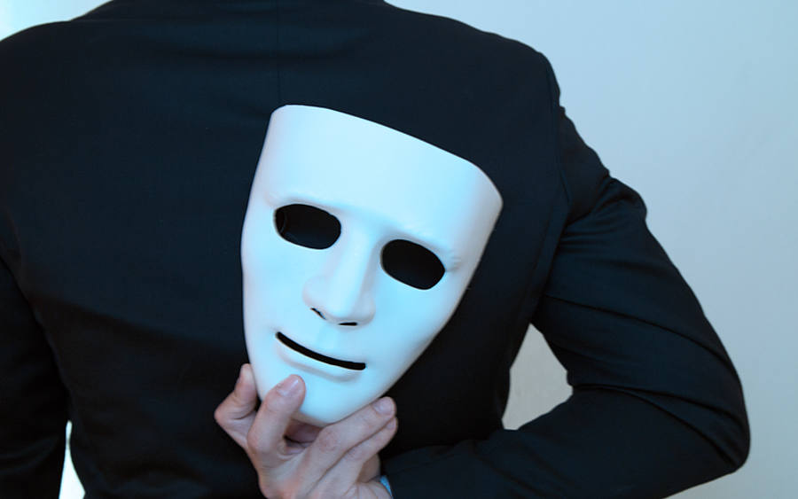Ein Geschäftsmann, der eine Maske hinter dem Rücken hält.