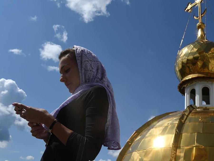 Eine Frau schaut auf dem Dach der orthodoxen Kathedrale von St. Theodor Uschakow in Saransk, Russland, auf ihr Smartphone. Foto: Marcus Brandt/dpa