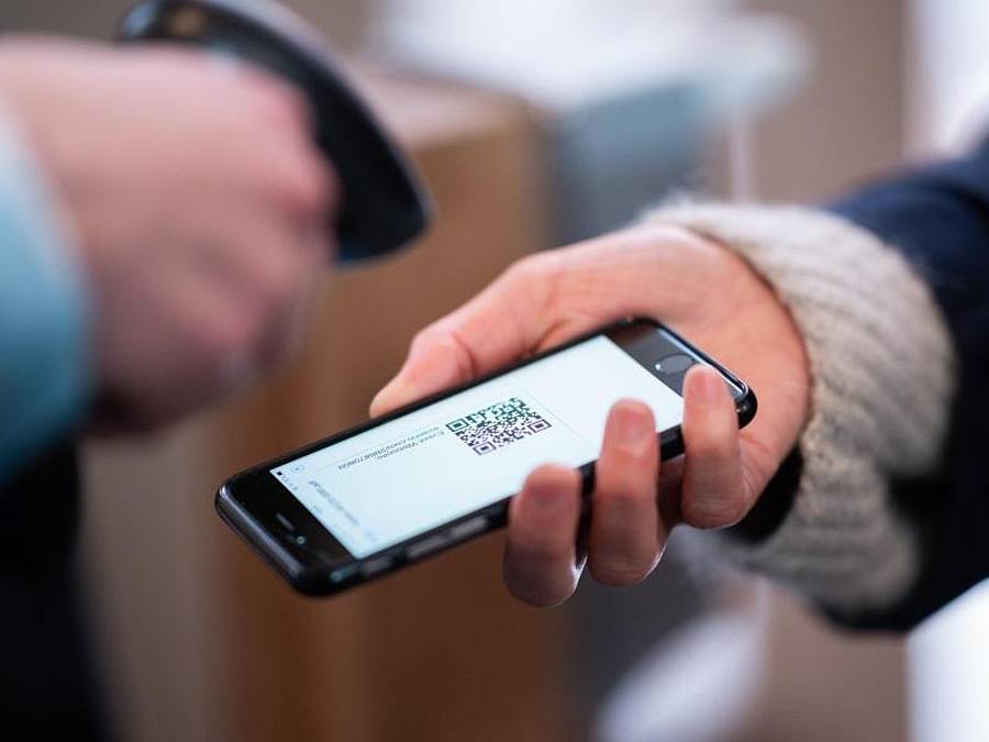 Eine Frau lässt am Eingang eines Corona-Schnelltest-Zentrums einen QR-Code auf ihrem Smartphone abscannen. Foto: Daniel Reinhardt/dpa