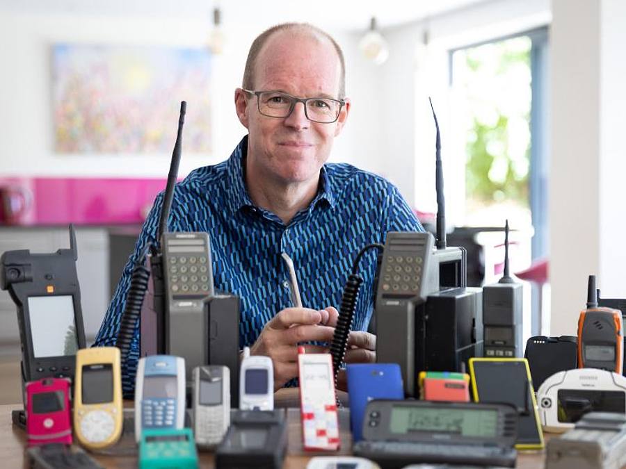 Auf dem vom Mobile Phone Museum herausgegebenen Foto sitzt Ben Wood, Gründer des Museums und Analyst des Unternehmens CCS Insight, hinter einigen der über 2.000 einzigartigen Mobiltelefone, die Teil des Online-Museums sein werden. Foto: Mobile Phone Mus