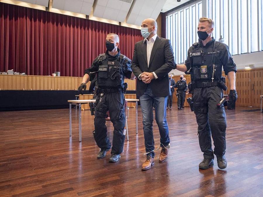 An Händen und Füßen gefesselt ist einer der Hauptangeklagten, den bewaffnete Polizisten in die zu einem Gerichtssaal umfunktionierte Kongresshalle in Gießen bringen. Foto: Boris Roessler/dpa