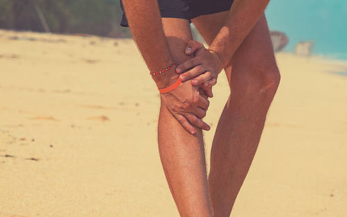 Läufer hält sich das Knie am Strand