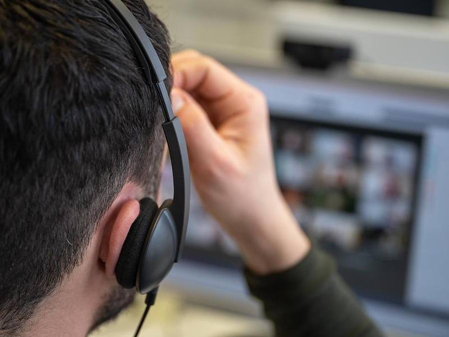 Ein junger Mann, der ein Headset trägt, nimmt an einer Videokonferenz teil. Foto: Sebastian Gollnow/dpa