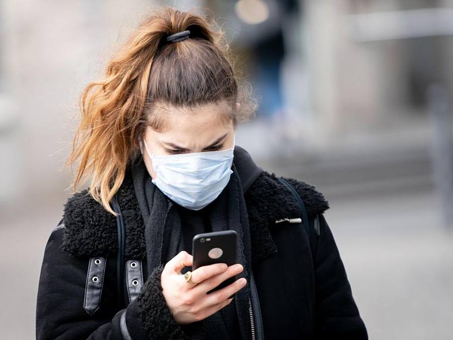 Frau mit Mundchsutz schaut auf Smartphone. Foto: Kay Nietfeld/dpa