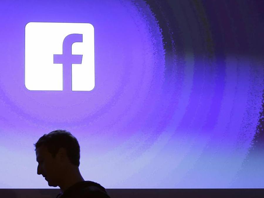 Der Schatten des Chefs: Mark Zuckerberg geht am Firmensitz an einem leuchtenden Facebooklogo vorbei.