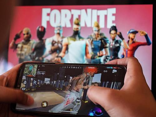 Ein Kind spielt ein Spiel auf einem Mobiltelefon mit einem Bild des Fortnite-Spiels auf dem Computerbildschirm im Hintergrund. (Archivbild). Foto: Herwin Bahar/ZUMA Wire/dpa