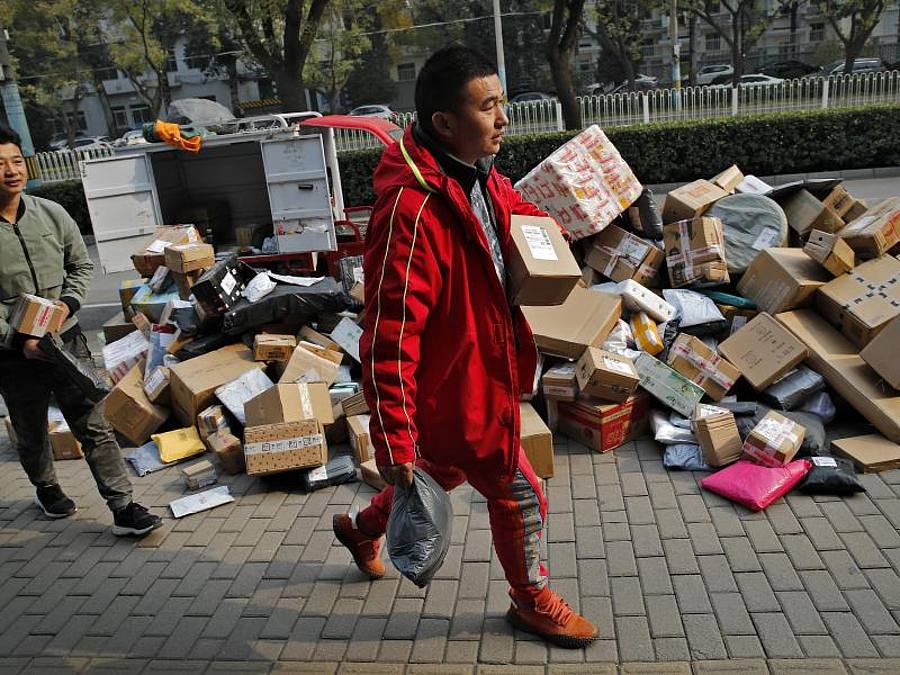 Zusteller sortieren Pakete, die sich an einem Abholpunkt in der Nähe eines Wohnhauses in Peking stapeln. Foto: Andy Wong/AP/dpa