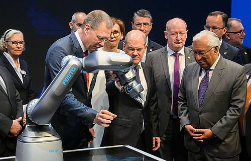 Bundeskanzler Olaf Scholz (M, SPD) und Antonio Costa (r), Premierminister von Portugal, betrachten neben Oliver Jung, Vorstandsvorsitzender Festo beim Eröffnungsrundgang auf der Hannover Messe 2022 einen Roboter mit pneumatischem Antrieb.