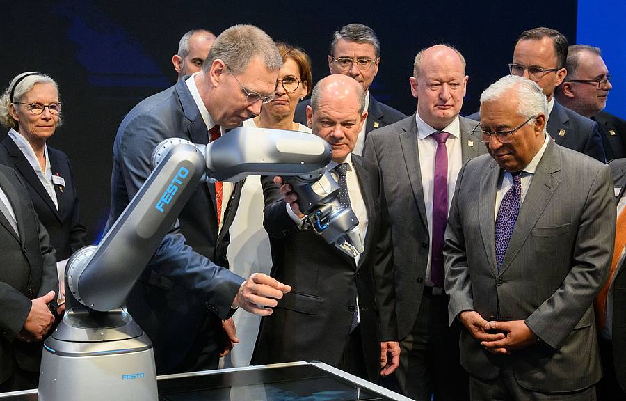 Bundeskanzler Olaf Scholz (M, SPD) und Antonio Costa (r), Premierminister von Portugal, betrachten neben Oliver Jung, Vorstandsvorsitzender Festo beim Eröffnungsrundgang auf der Hannover Messe 2022 einen Roboter mit pneumatischem Antrieb.
