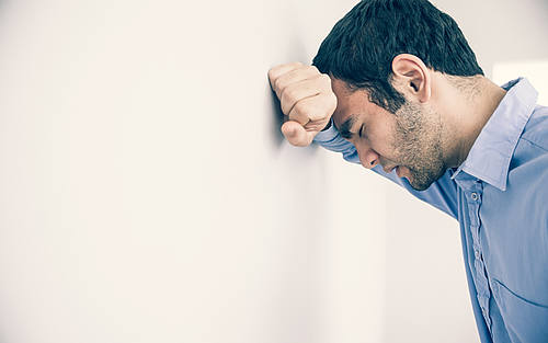 Ein depressiver Mann lehnt an einer Wand.