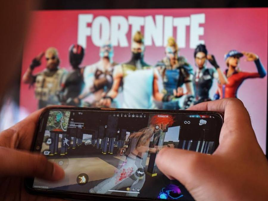 Ein Kind spielt ein Spiel auf einem Mobiltelefon mit einem Bild des Fortnite-Spiels auf dem Computerbildschirm im Hintergrund. Kalifornien. Foto: Herwin Bahar/ZUMA Wire/dpa