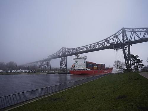 Ein Containerschiff im Frühnebel auf dem Nord-Ostsee-Kanal unter der Rendsburger Hochbrücke Anfang März 2022. Foto: Marcus Brandt/dpa