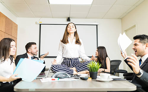 Frau sitzt im Büro und meditiert auf dem Schreibtisch