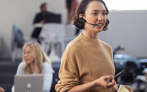 Eine junge Frau steht im Büro und hat ein Headset auf dem Kopf.