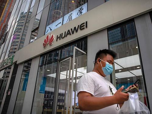 Ein Mann mit Gesichtsmaske schaut auf sein Smartphone, als er an einem Huawei-Laden in Peking vorbeigeht. Foto: Mark Schiefelbein/AP/dpa