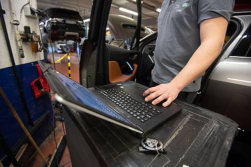 Ein KFZ-Mechaniker wartet in einer KFZ-Werkstatt einen elektrisch angetriebenen Jaguar I-Pace Vorführwagen.