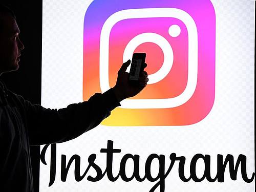 Ein Mann hält ein Smartphone vor einem Monitor mit dem Logo von Instagram. Foto: Carsten Rehder/dpa