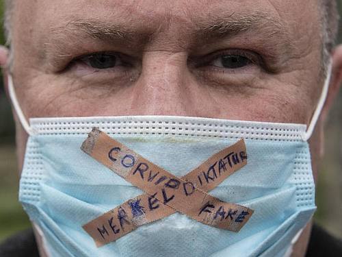 Ein Teilnehmer einer Kundgebung gegen die Corona-Maßnahmen der Regierung trägt einen Mundschutz mit der Aufschrift "Merkel-Diktatur - Covid-Fake". Foto: Boris Roessler/dpa