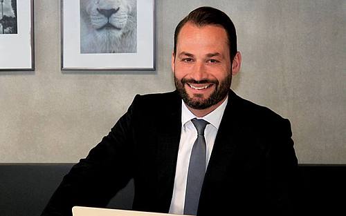 Geschäftsmann sitzt im Anzug vor einer Wand mit Bildern