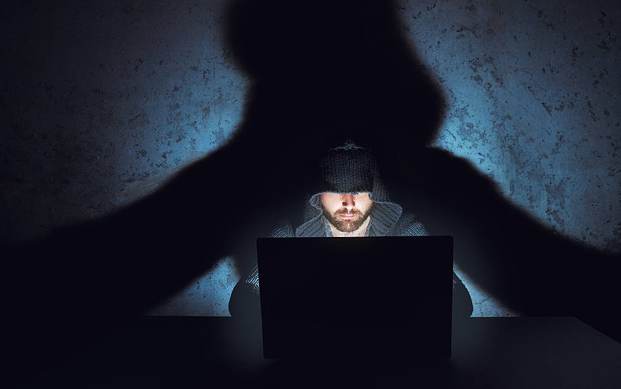 Hacker sitzt im Lichtkegel vor einem Laptop