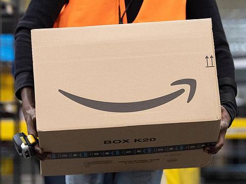 Ein Sortiermitarbeiter von Amazon trägt in einem Verteilzentrum ein Paket. Foto: Sebastian Kahnert/dpa-Zentralbild/dpa