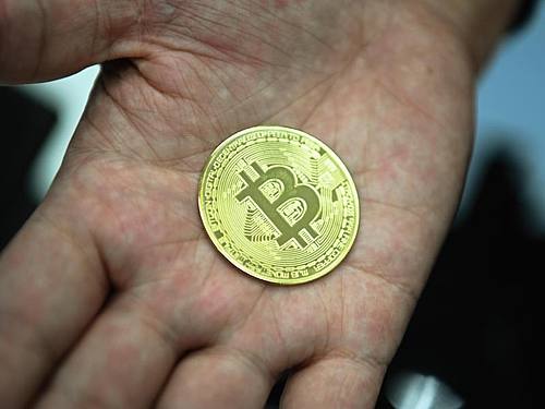 Ein Mann hält eine nachgemachte Münze mit dem Bitcoin-Logo in den Händen. Foto: Nicolas Armer/dpa