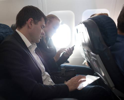 Geschäftsleute arbeiten mit Mobilgeräten im Flugzeug