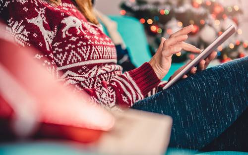 Ein Frau im Weihnachtspullover surft mit einem Tablet