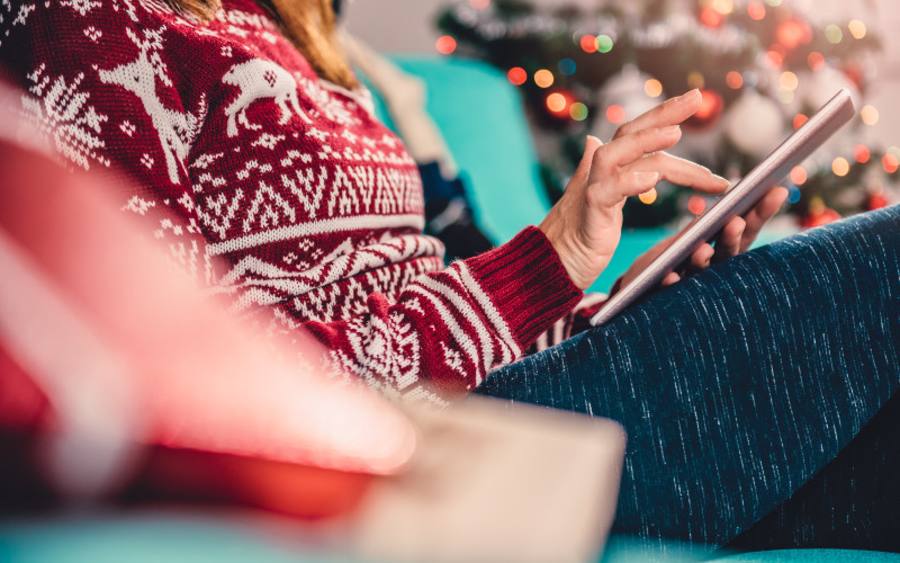 Ein Frau im Weihnachtspullover surft mit einem Tablet