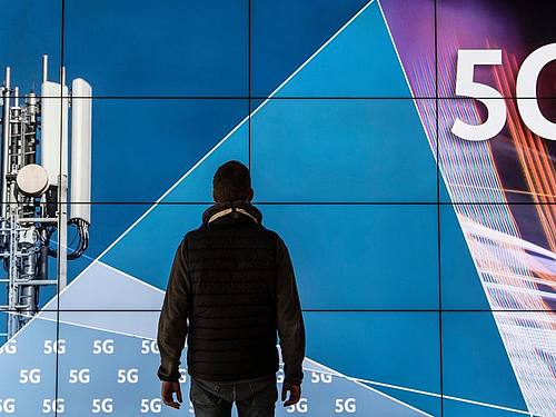 Ein Mann steht im Gebäude der Bundesnetzagentur vor einer Leinwand mit der Aufschrift „5G“. ((Foto: Boris Roessler))