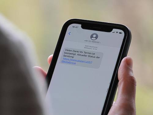 Eine Frau hält ein Smartphone in ihrer Hand, auf dessen Display eine Betrugs-SMS zu lesen ist. Foto: Wolf von Dewitz/dpa