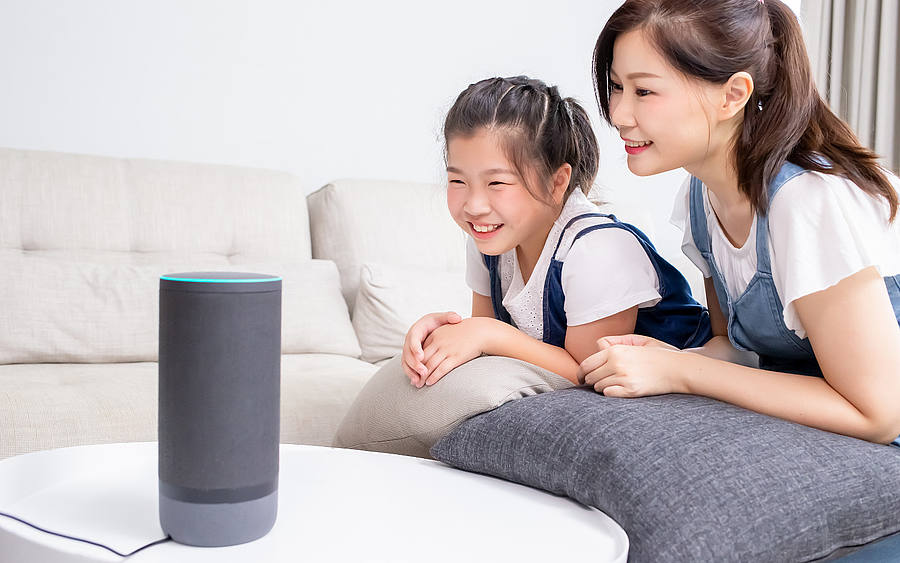 Asiatische Mutter mit Tochter nutzt Sprachassistent