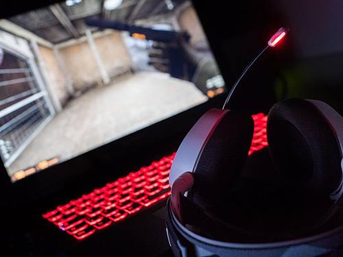 Ein Gaming-Kopfhörer liegt auf einem Gaming-Laptop auf einem Tisch. Foto: Lino Mirgeler/dpa