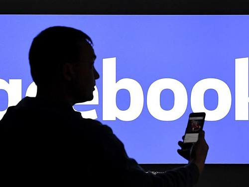 Ein Mann mit Smartphone steht vor einem Monitor mit dem Logo von Facebook. Foto: Carsten Rehder/dpa