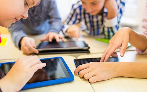 Kinder sitzen am Tisch und nutzen Tablets